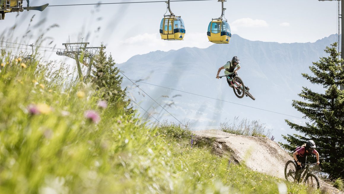Mountainbiker auf Trail im Sommer mit Seilbahn im Hintergrund