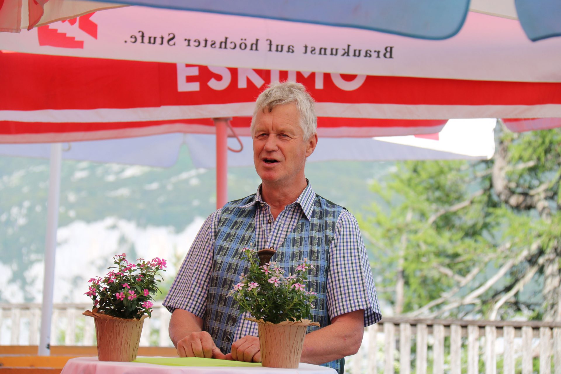 Älterer Mann in Tracht hält in Lokal auf Terrasse Ansprache