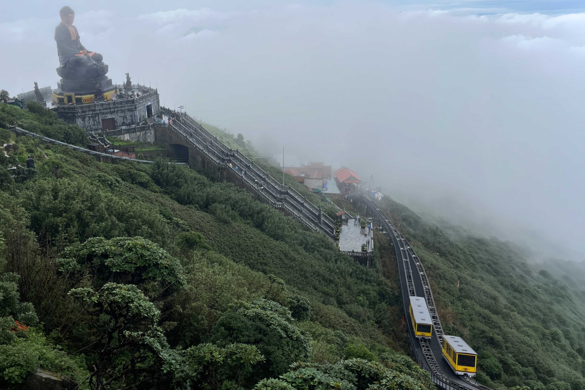 Tempelanlage mit Buddha-Statue und Standseilbahninfrastruktur im Nebel