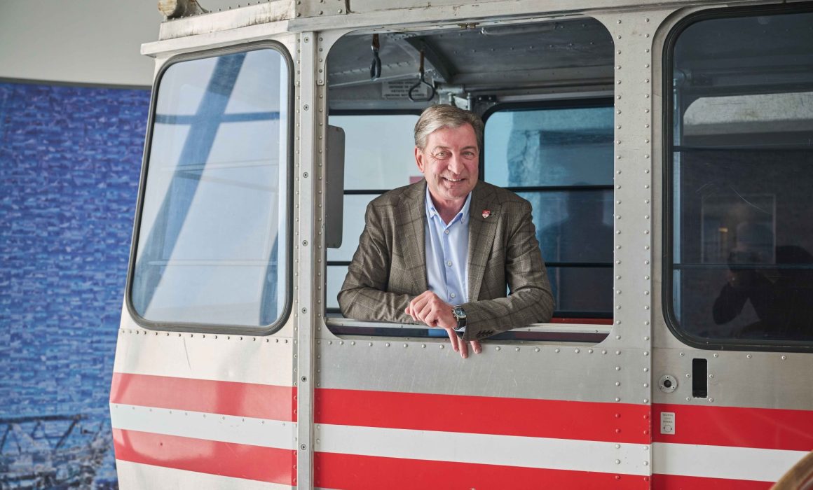 Mann im Anzug postiert in Seilbahnkabine und schaut aus geöffnetem Fenster