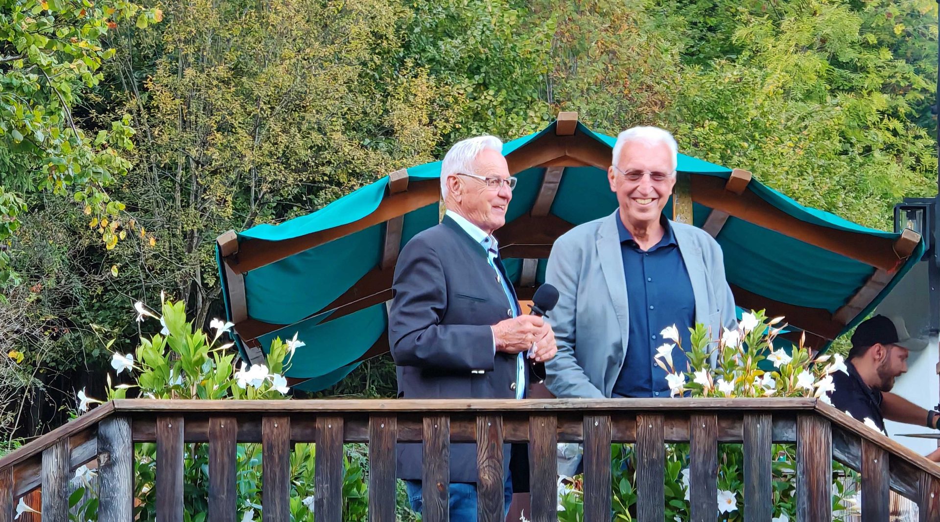 Zwei ältere Herren im Anzug lachen und stehen vor Balkongeländer
